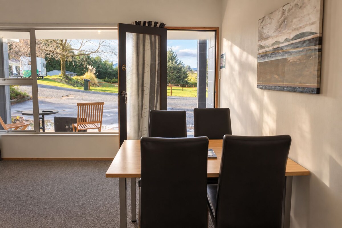 A room with a table and chairs, a window with a view of the outside, and a painting on the wall.