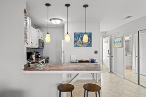 A modern kitchen with a curved island, pendant lighting, and a painting on the wall. - Sandpiper Cove Unit 8248 Pet-Friendly | 3-minute walk to the beach (Destin)