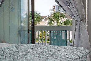 A bedroom with a large bed, a sliding glass door leading to a balcony, and a view of palm trees and buildings. - Sandpiper Cove Unit 8248 Pet-Friendly | 3-minute walk to the beach (Destin)
