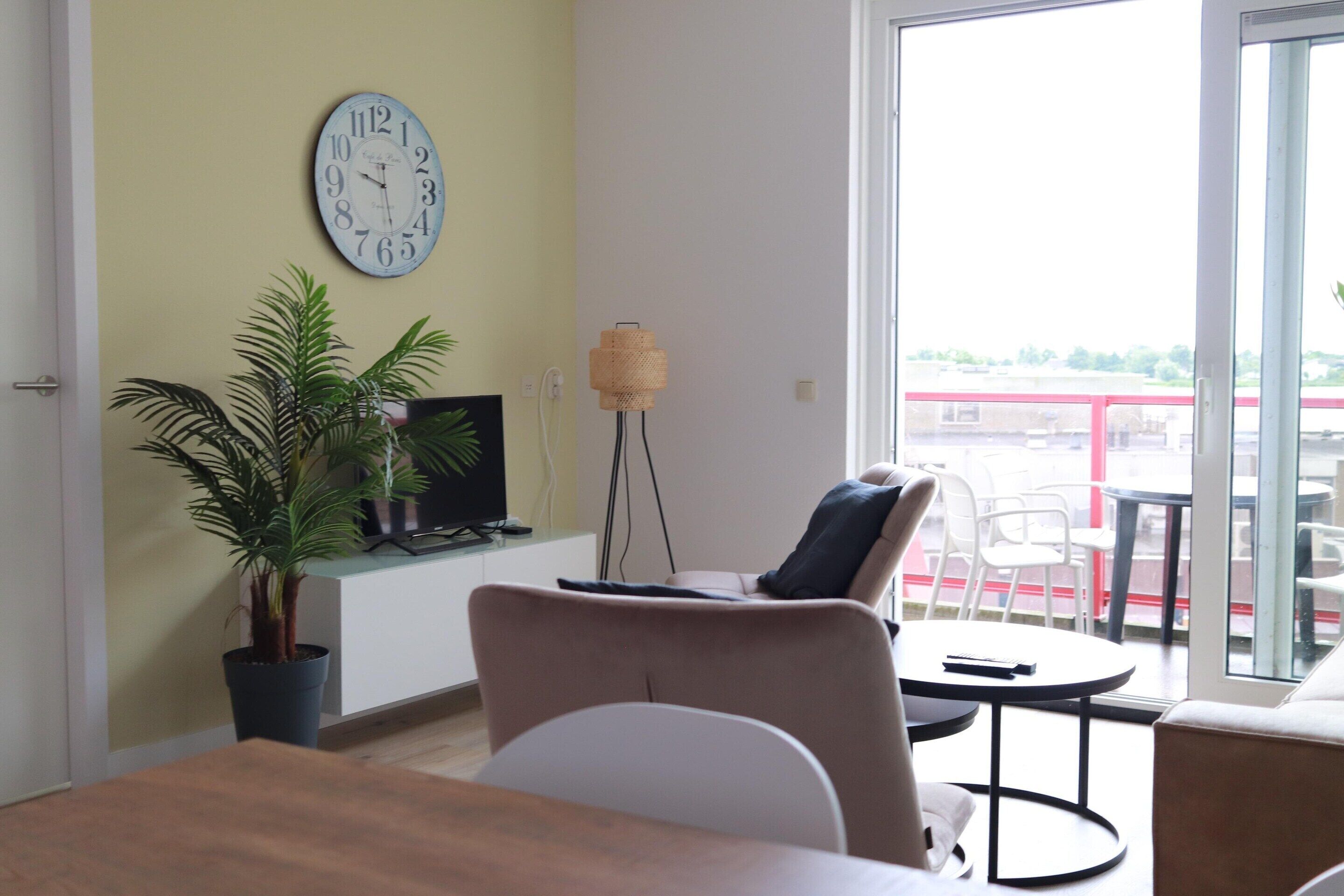 Una sala de estar con sofá, una mesita, una planta en maceta, televisor y un reloj de pared.