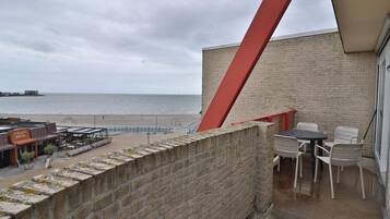 Un balcon avec vue sur la plage et la mer, un mur en briques et des sièges d’extérieur.