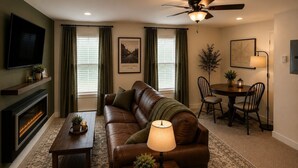 A living room with a leather sofa, a fireplace, a television, and a dining area with a table and chairs. - The Washington Lofts (Ellicottville)