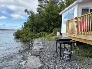 A waterfront property with a deck, grill, propane tank, and a view of the water. - Lakefront Cottage in Scenic Guffin Bay (Chaumont)