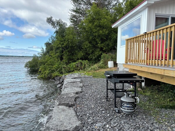 A waterfront property with a deck, grill, propane tank, and a view of the water.