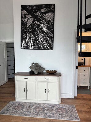 A room with a white cabinet, a rug, and a black and white artwork on the wall.