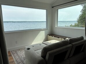 A room with a view of a body of water through large windows, a gray sofa, and a patterned rug.