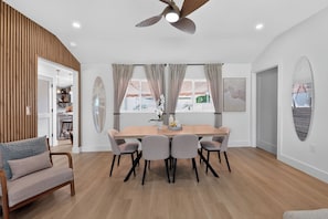 A modern dining area with a wooden table and chairs, a ceiling fan, and a view of the outdoors. - Coastal - 3BR King Suite - 15 Min to Anna Maria Island & IMG (Bradenton)