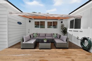 A covered outdoor seating area with a wicker sofa and a coffee table, a potted plant, and a hose on the deck. - Coastal - 3BR King Suite - 15 Min to Anna Maria Island & IMG (Bradenton)