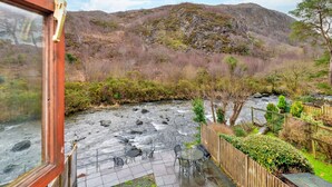 A riverside patio with outdoor seating and a view of a mountainous landscape. - Beddgelert Cottage Escape (Caernarfon)
