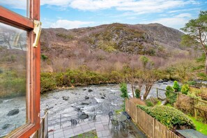 Eine Terrasse am Flussufer mit Sitzgelegenheiten im Freien und Blick auf eine gebirgige Landschaft.