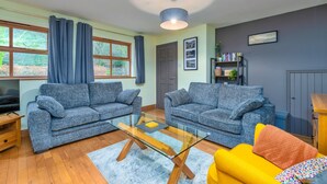 A living room with two grey sofas, a glass coffee table, a yellow armchair, and a bookshelf. - Beddgelert Cottage Escape (Caernarfon)