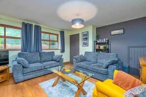 Ein Wohnzimmer mit zwei grauen Sofas, einem Glastisch, einem gelben Sessel und einem Bücherregal.