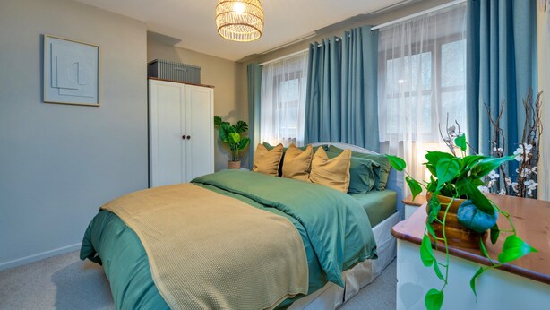 A bedroom with a bed, a bedside table with a plant, a wardrobe, and a window with curtains. - Beddgelert Cottage Escape (Caernarfon)