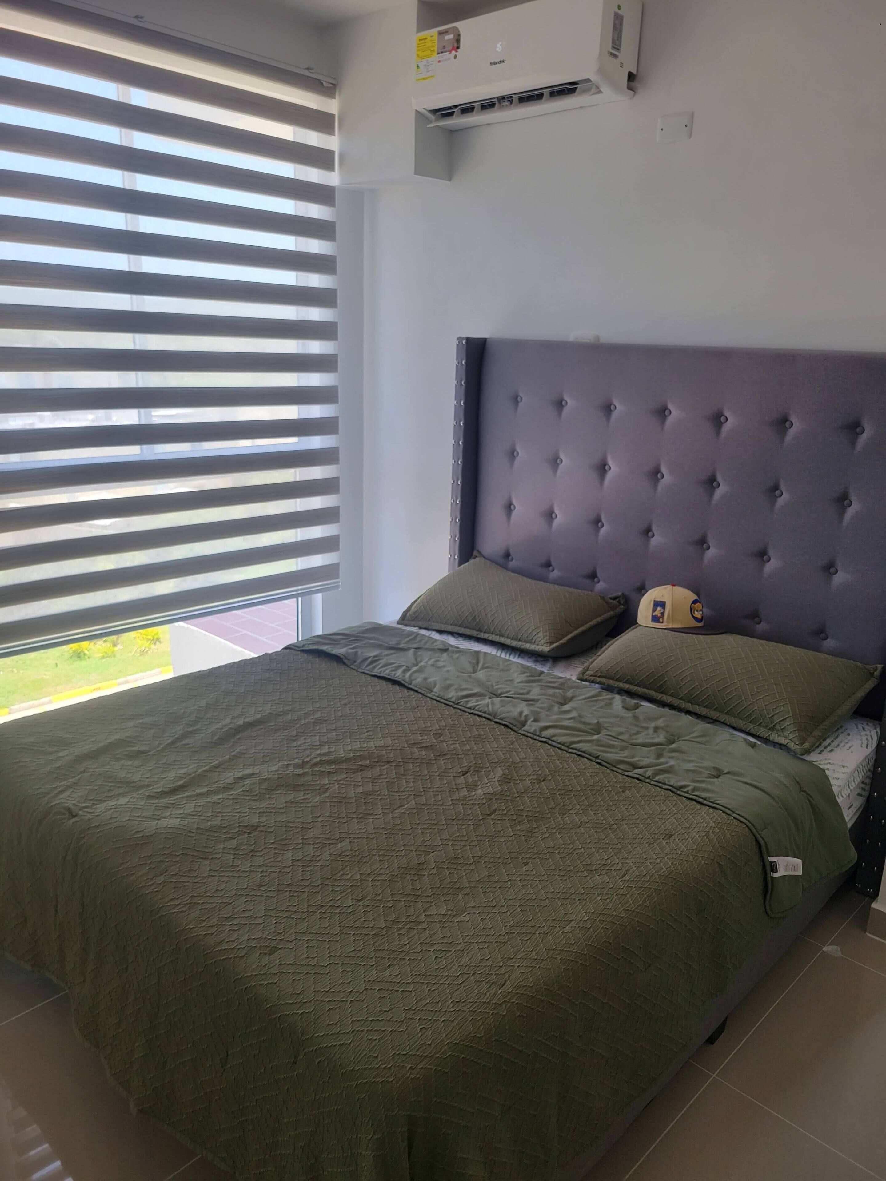 Quarto com cama, cabeceira e janela com persianas.