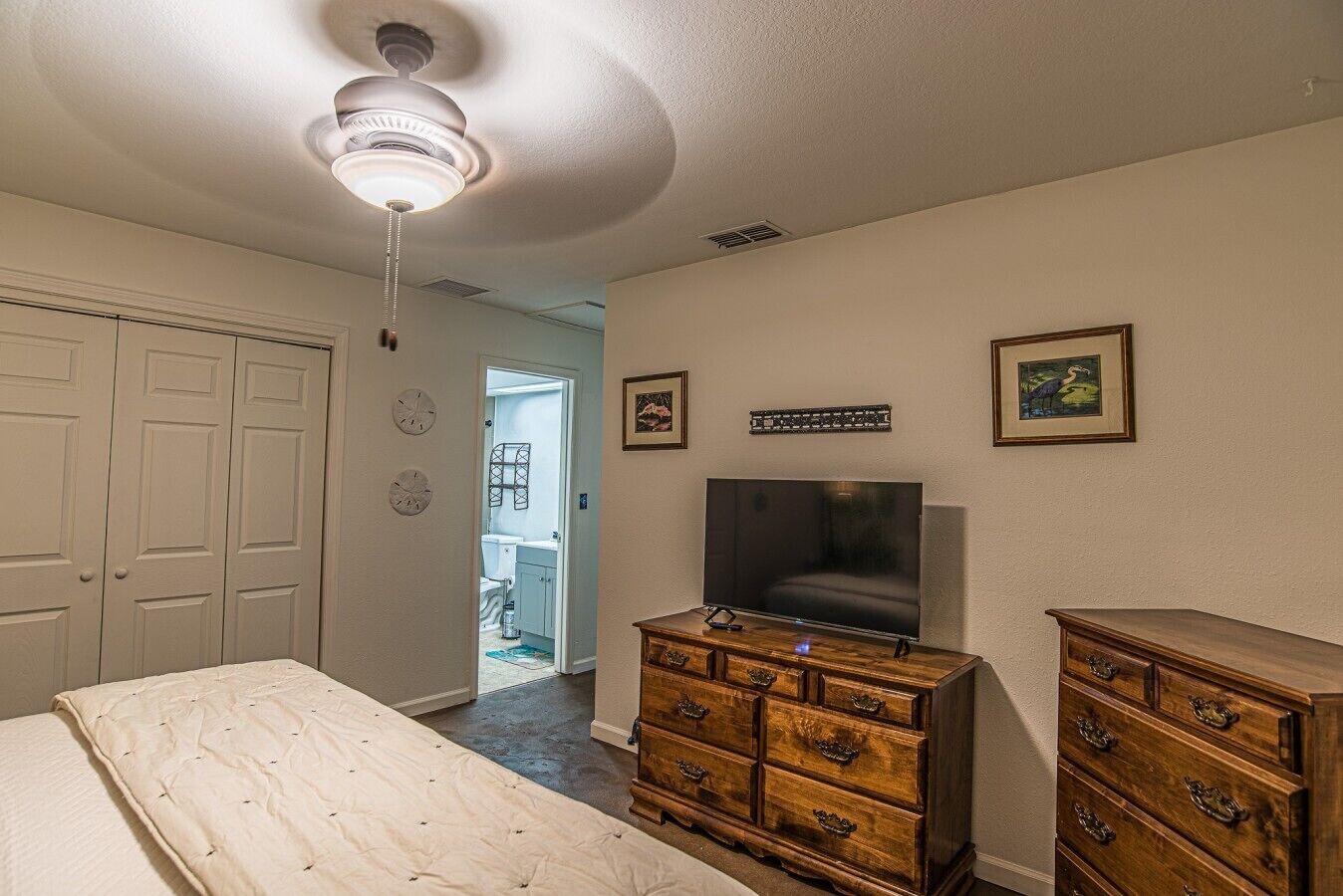 A bedroom with a bed, a dresser, a television, and a ceiling fan.