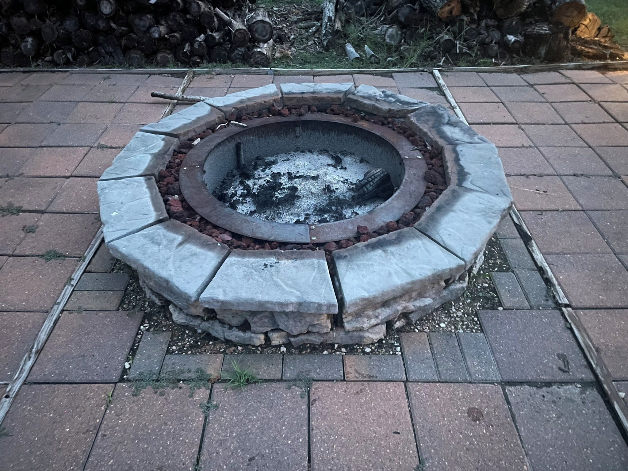 En rund stenläggning som utgör en eldstad, med en metallkant, omgiven av ett stenlagt område.