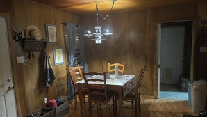 A dining area with a wooden table and chairs, a chandelier, and a window with curtains. - Wooded 2 bedroom 2 bath Cabin retreat near Lake Somerville Texas (Somerville)