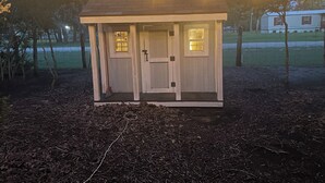 A small wooden structure with a door and windows, surrounded by trees and a grassy area. - Wooded 2 bedroom 2 bath Cabin retreat near Lake Somerville Texas (Somerville)