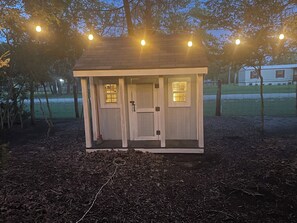 Eine kleine Holzhütte mit Tür und Fenstern, umgeben von Bäumen und einer Wiese.