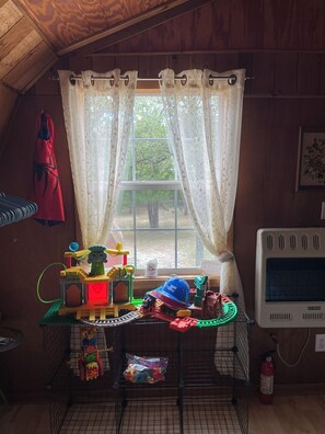 Ein Zimmer mit Fenster, Tisch mit Spielzeug, eine rote Jacke und ein weißes Gerät.