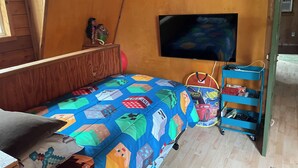 A room with a bed, a television mounted on the wall, and a blue storage cart with items on it. - Wooded 2 bedroom 2 bath Cabin retreat near Lake Somerville Texas (Somerville)