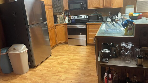 A kitchen with wooden cabinets, stainless steel appliances, and a countertop with various items. - Wooded 2 bedroom 2 bath Cabin retreat near Lake Somerville Texas (Somerville)