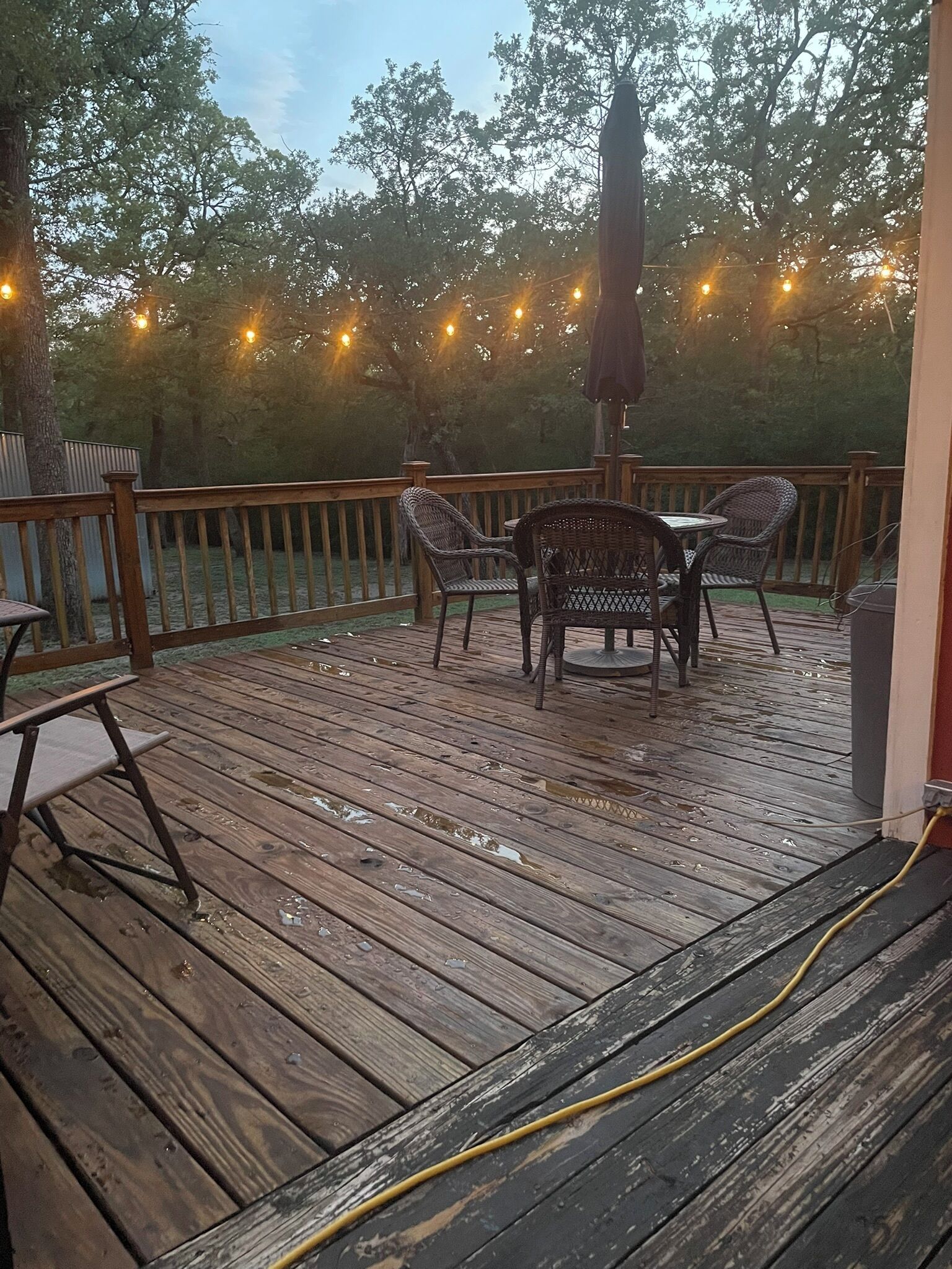 A wooden deck with outdoor furniture, including a table and chairs, and a string of lights in the background.