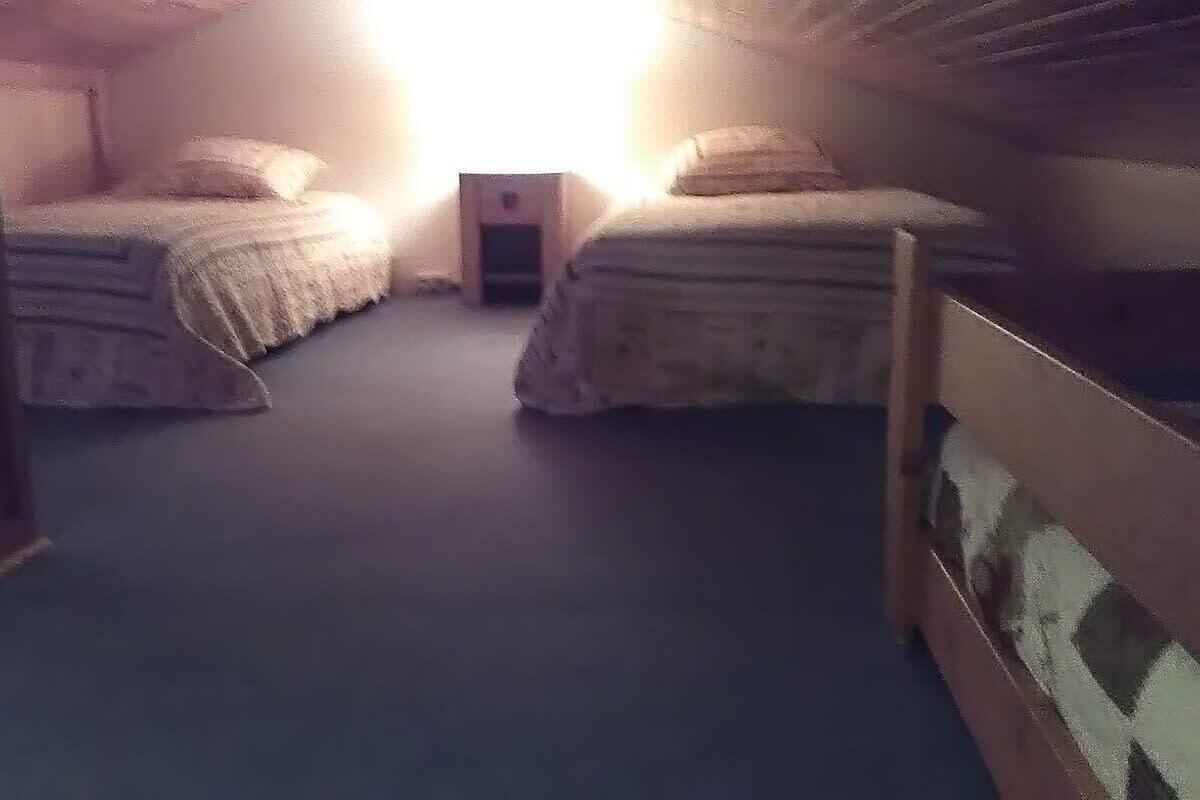 A room with two beds, a small table, and a slanted ceiling.