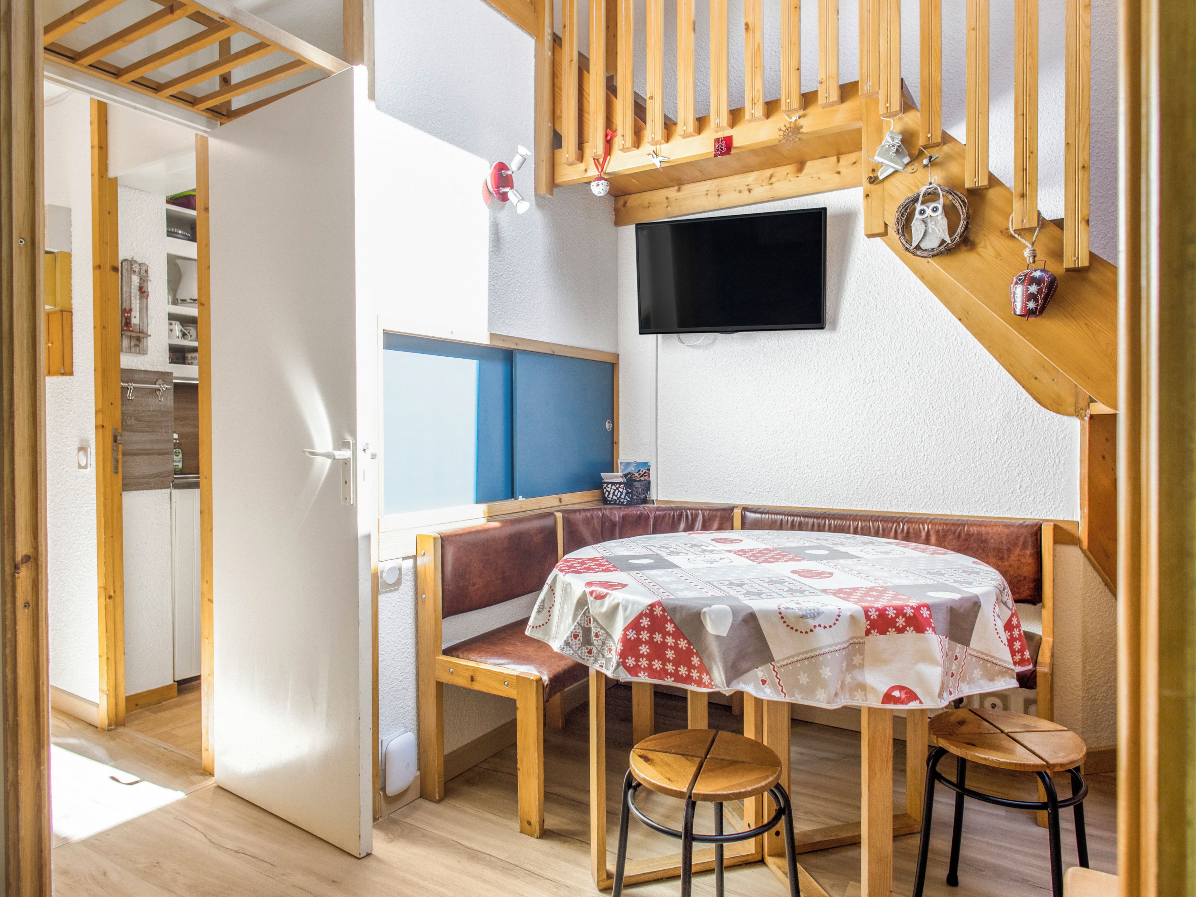 Een gezellige kamer met een houten bank, een tafel met een tafelkleed en een aan de muur bevestigde televisie.