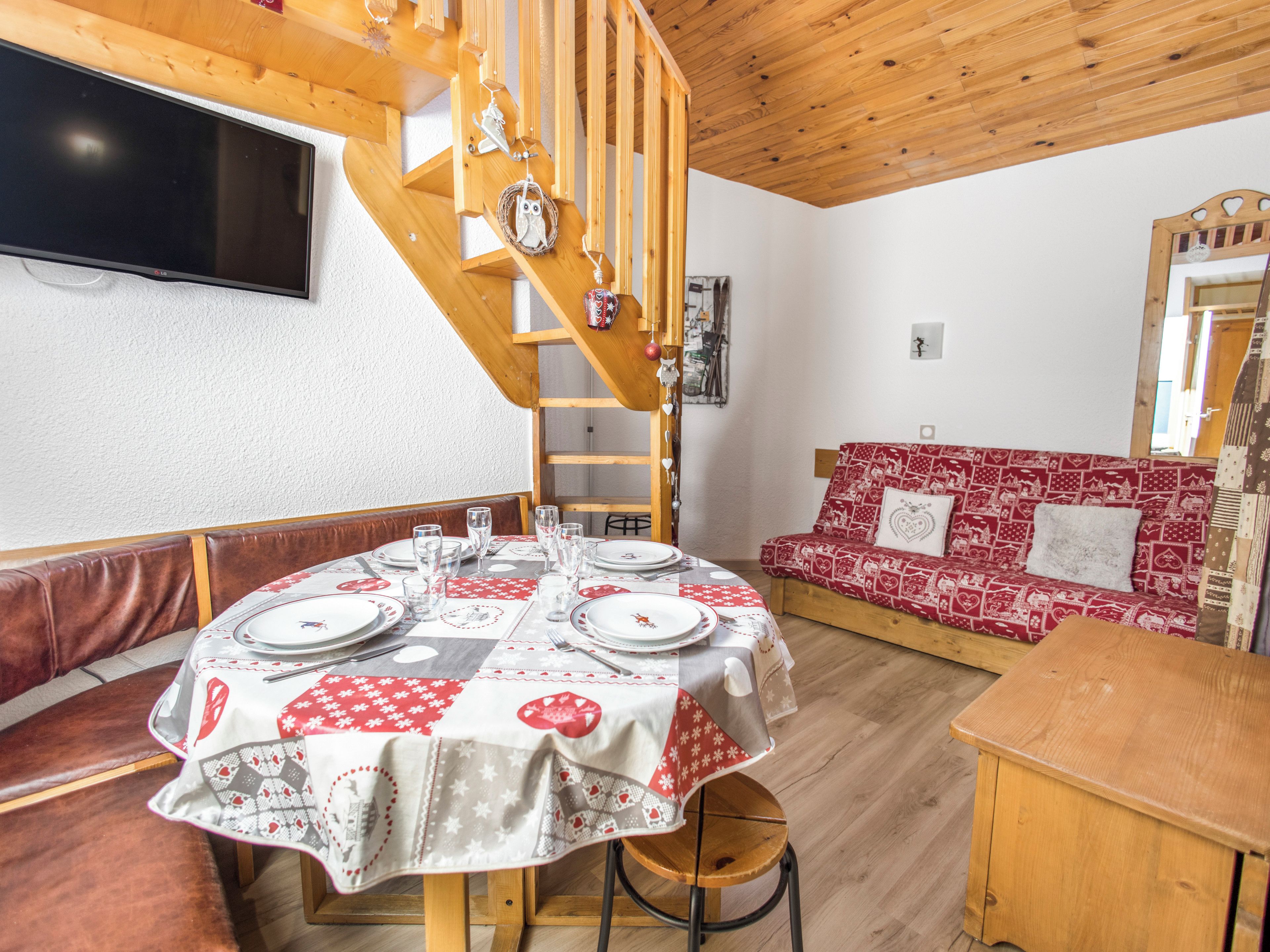 En matplats med ett runt bord för fyra personer, en trätrappa och en röd soffa med mönster.