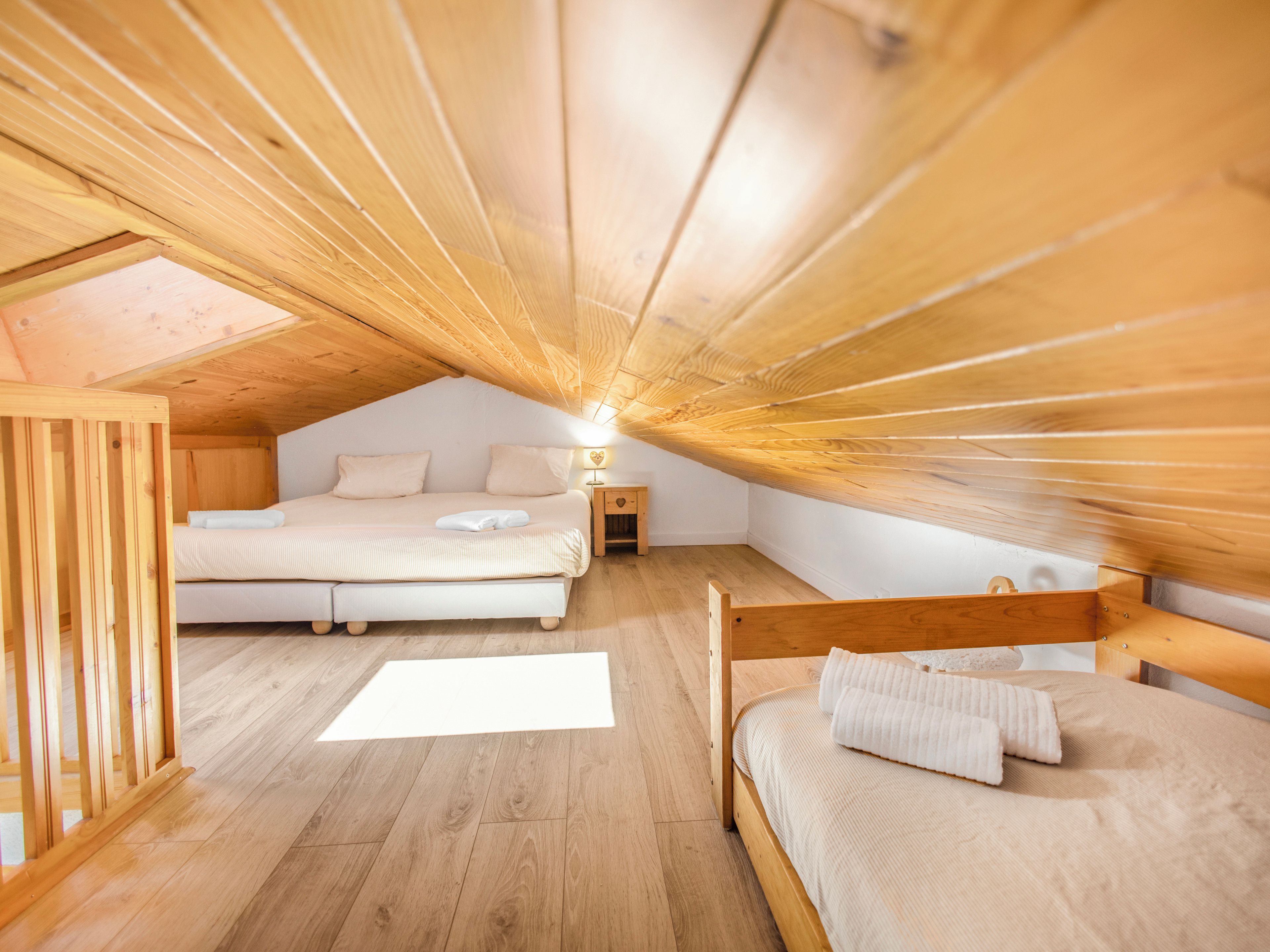 Une pièce avec un plafond en pente, un plancher en bois, deux lits, une table de chevet et un puits de lumière.