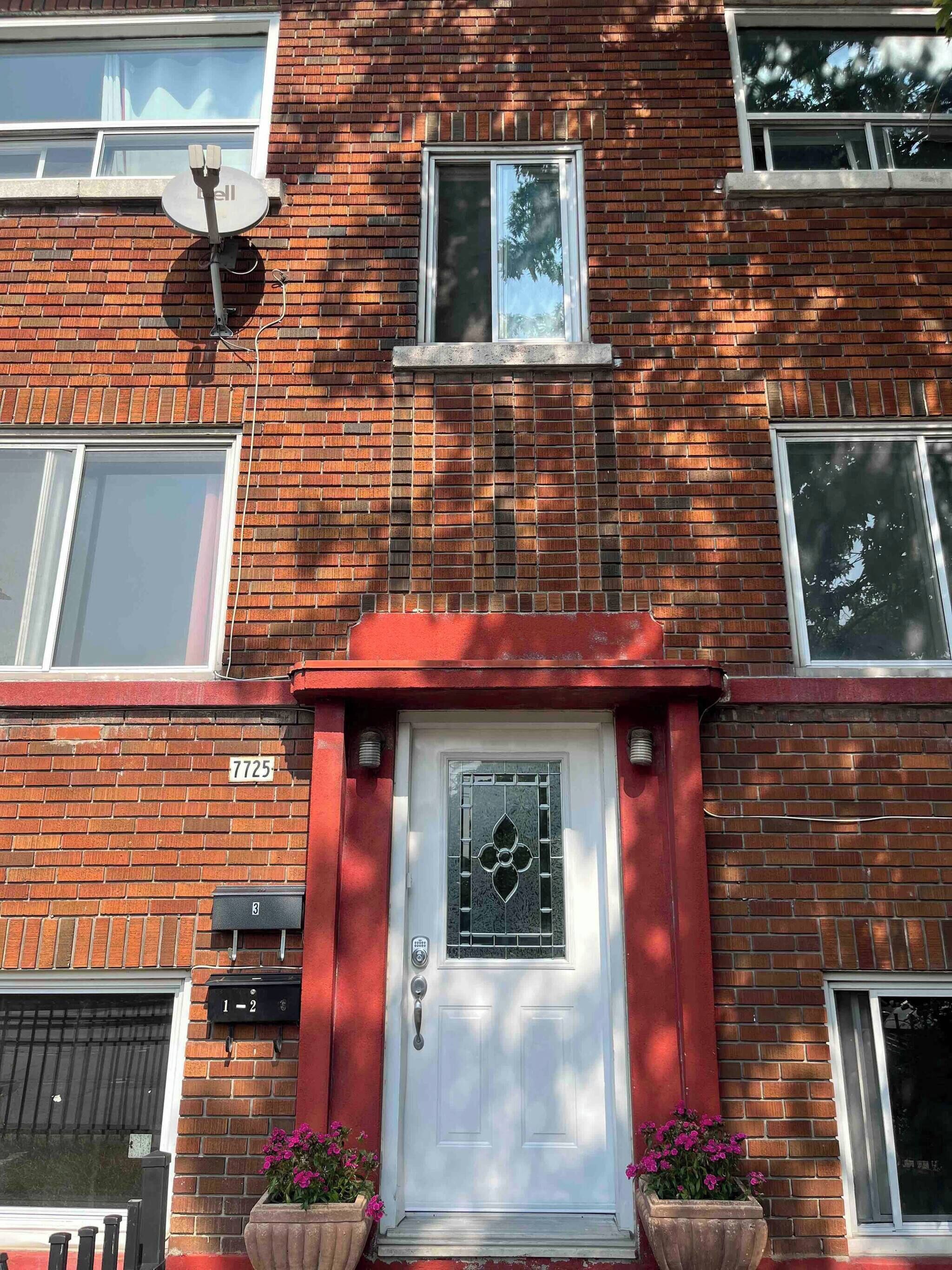 A red brick building with a white door, a satellite dish, and a number '7725' on the wall.