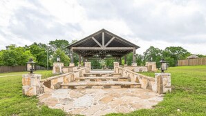 A stone pavilion with a roof, surrounded by a stone pathway leading to it. - Premium Cabin - Family Cabin Rental Sleeps 8-10 (Willis)
