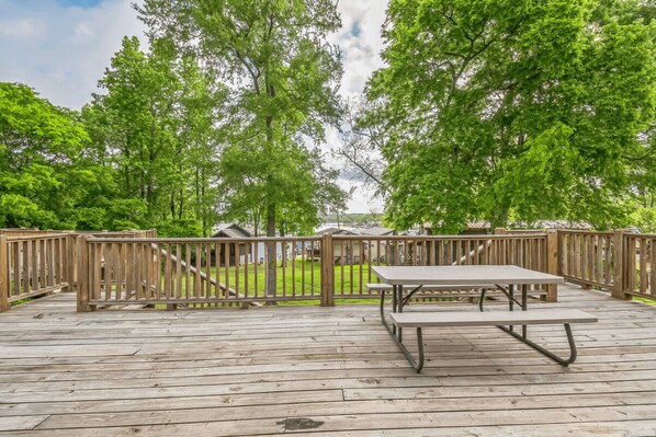 A wooden deck with picnic tables and a view of a grassy area with trees.