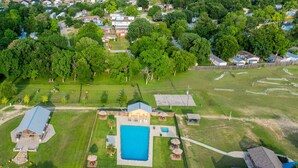 An aerial view of a residential area with a large swimming pool, multiple houses, and a fenced sports field. - Premium Cabin - Family Cabin Rental Sleeps 8-10 (Willis)