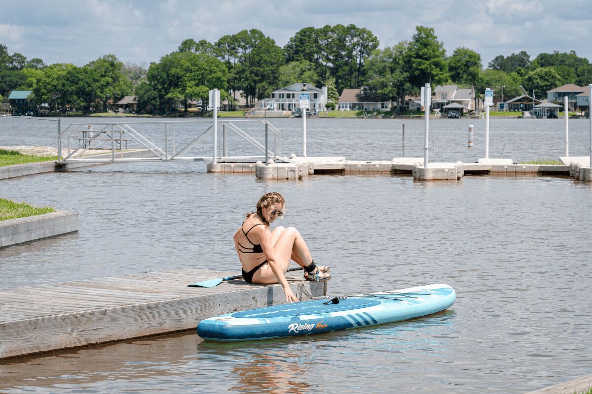A person sitting on a dock by a calm body of water with a kayak nearby.