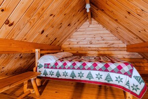 Ein Schlafzimmer im Blockhaus mit schrägem Dach, einem Bett mit gemustertem Überwurf und einer Holzbank.