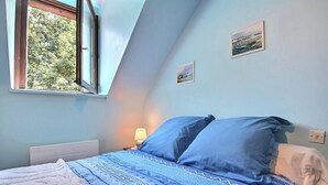 Un dormitorio con cama, una ventana y dos cuadros colgados en la pared.