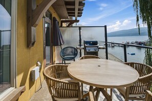 Ein Balkon mit rundem Tisch und Korbstühlen, mit Blick auf ein Gewässer mit Booten und einer Anlegestelle.