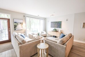 A modern living room with a sofa set, a coffee table, and a side table. There is a window with blinds, a painting on the wall, and a cabinet with decorative items. - 2-floor Lakeview Oasis at Barona Beach Resort (West Kelowna)