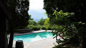 A swimming pool with a wooden deck, surrounded by lush greenery and a view of the sky. - Stunning Vineyard Estate House (Kelowna)