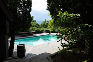 Ein Schwimmbecken mit Holzterrasse, umgeben von üppiger Vegetation und Blick zum Himmel.