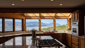 A kitchen with a large island, a gas stove, and a view of a lake and mountains. - Stunning Vineyard Estate House (Kelowna)