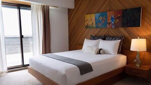 A hotel room with a large bed, a wooden headboard, a painting above the bed, a nightstand with a lamp, and a view through a sliding door. - Stunning Vineyard Estate House (Kelowna)