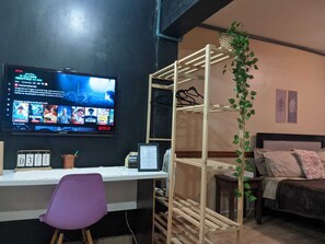 Une pièce comprenant un bureau, une chaise, un lit, un téléviseur et une plante.