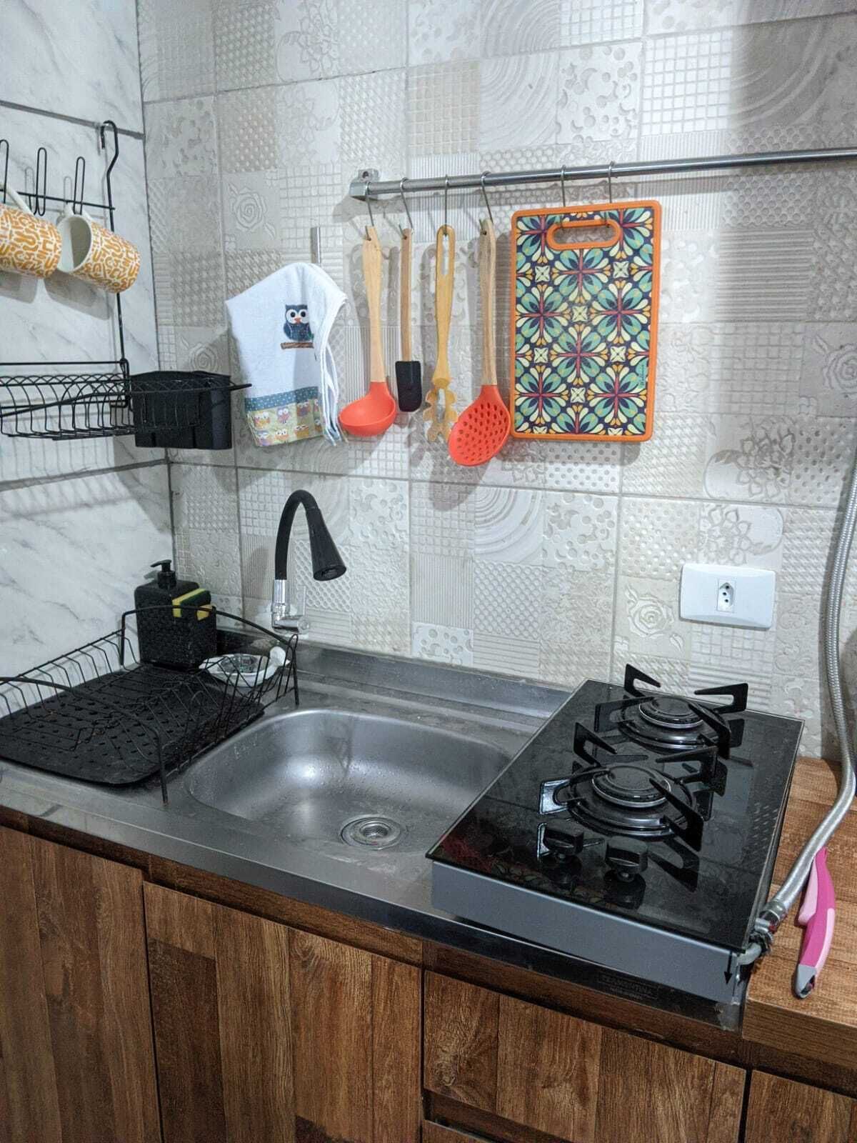 A kitchen with a gas stove, a sink, and various utensils hanging on the wall.