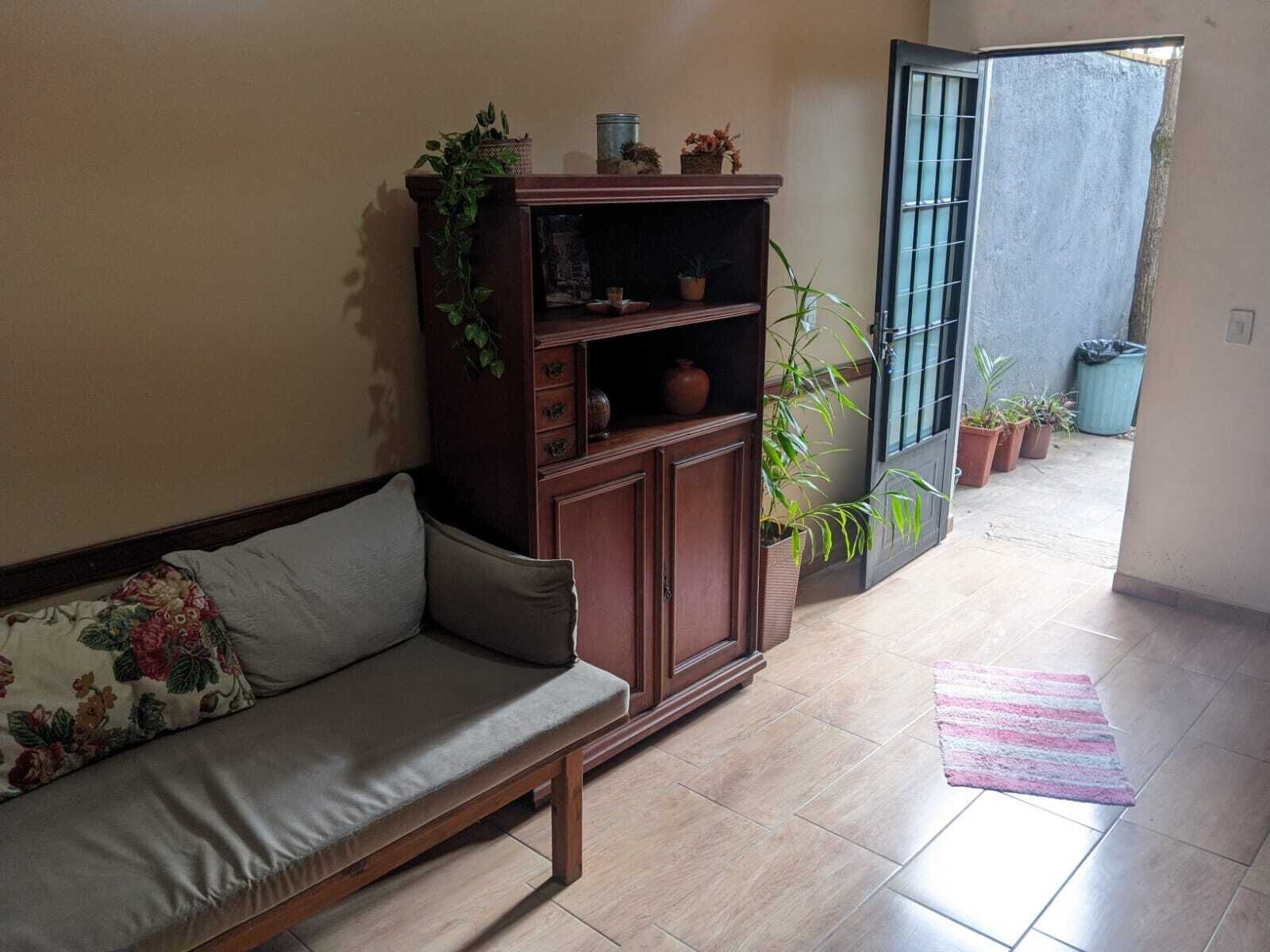 A living room with a sofa, a wooden cabinet with plants, and a tiled floor.