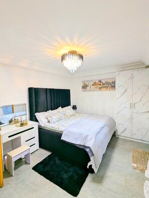 A bedroom with a bed, a desk, a chair, a wardrobe, a chandelier, and a cityscape painting. - STYLE AND COMFORT IN THE HEART OF THE CITY (LOME)