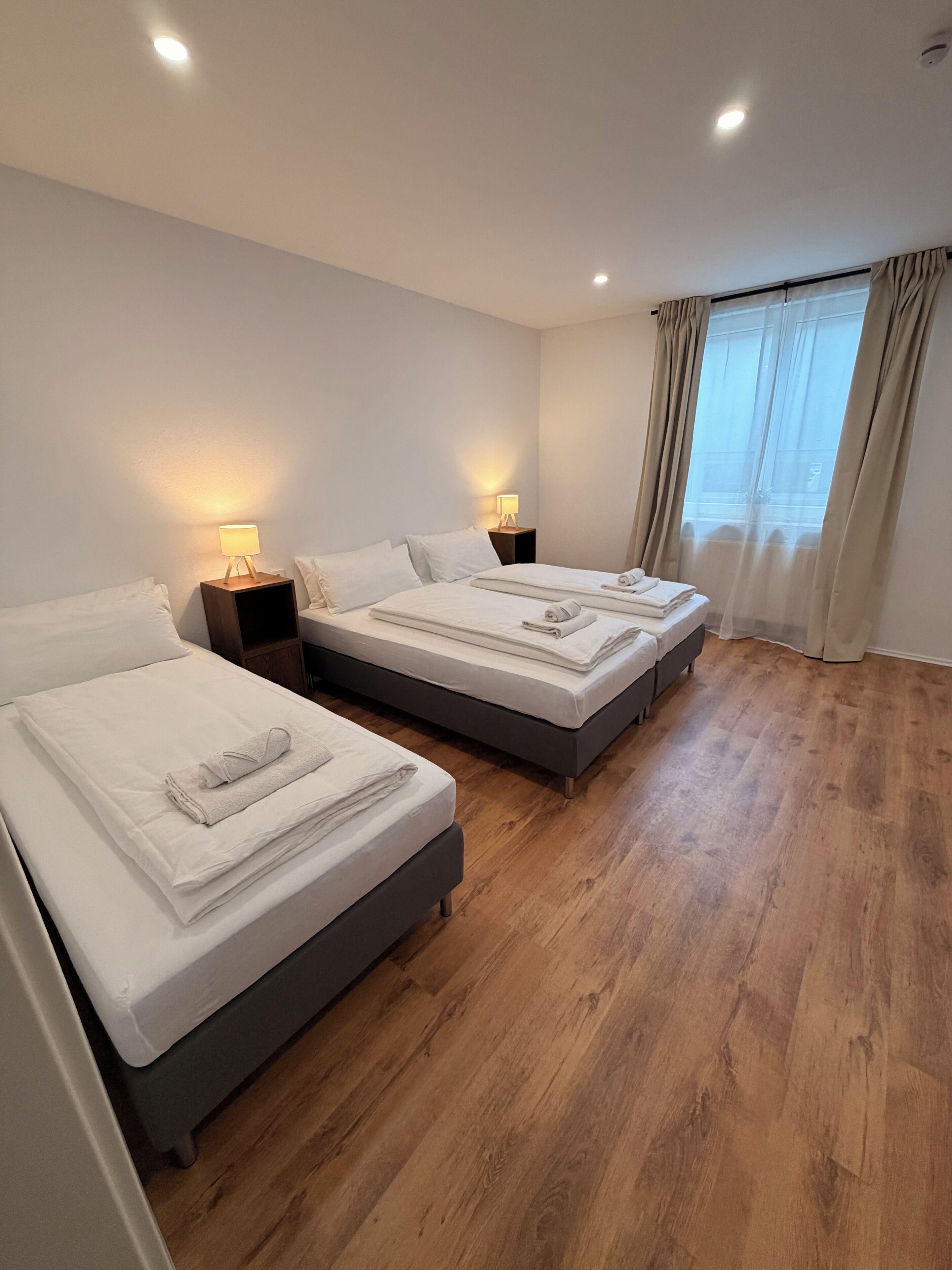 Ein Hotelzimmer mit zwei Betten, Holzboden und einem Fenster mit Vorhängen.