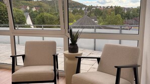 Una habitación con dos sillas, una planta en maceta y vistas a un lago y casas.